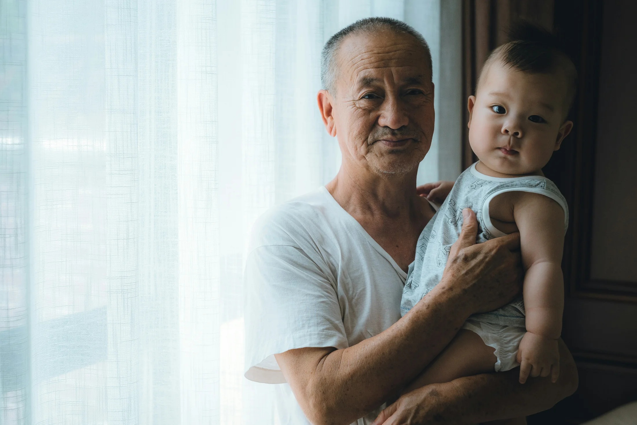 A grandfather holding his grandchild beside a softly lit window